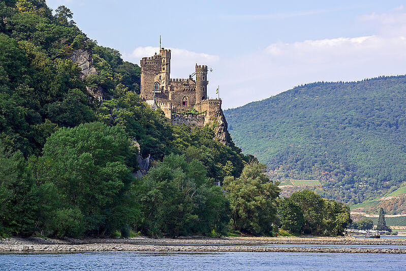 An einem Berghang steht eine Burg. Ein Fluss fließt durch das Tal.