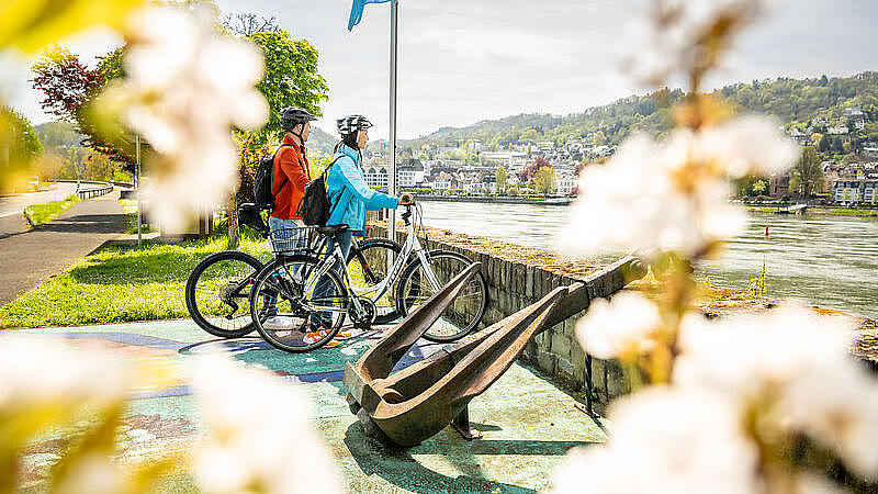 Two cyclists are standing by the river, enjoying the view.
