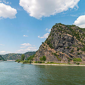 A large rock with tree growth is surrounded by water.