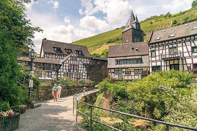 Ein Ort mit Fachwerkhäusern, einem Wanderweg und Weinbergen im Hintergrund.