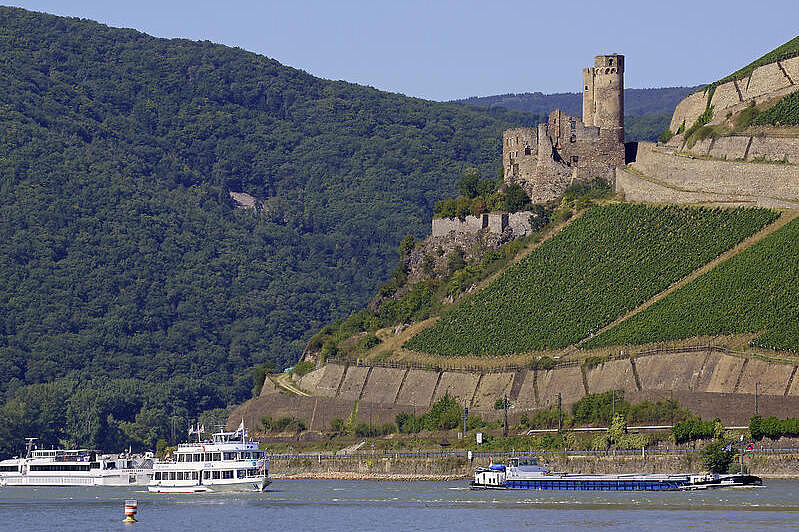 Auf einem Hügel befindet sich eine Ruine, und im Fluss davor sind drei Schiffe zu sehen.