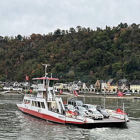 Die Fähre Loreley fährt vor dem Rheinufer über den Rhein.
