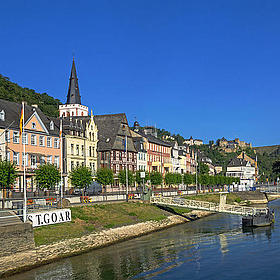 By a river with a bright blue sky, there is a small village with half-timbered houses.