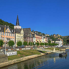 An einem Fluss mit strahlend blauem Himmel liegt ein kleines Dorf mit Fachwerkhäusern.