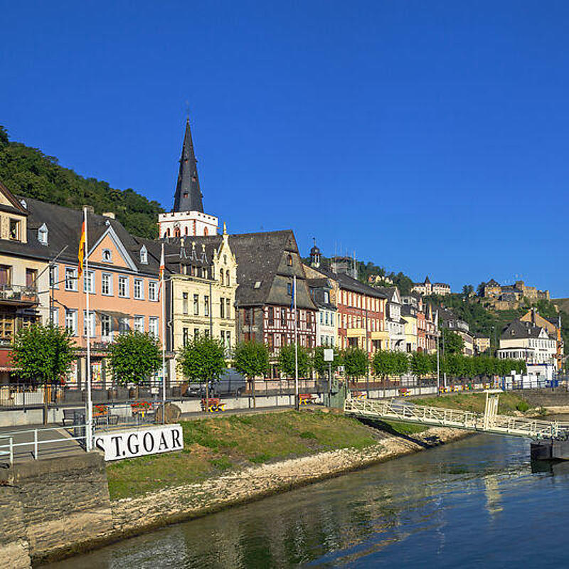 [Translate to Español:] By a river with a bright blue sky, there is a small village with half-timbered houses.