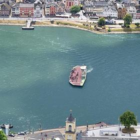 Two riverbanks, each with a small village, are visible. In the middle, a ferry is crossing the river.